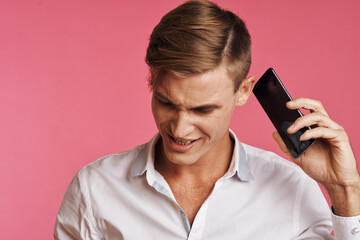 Fototapeta premium portrait of a man in a white shirt talking on the phone pink background