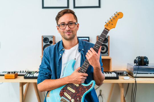 Male guitarist wearing eyeglasses holding guitar at home