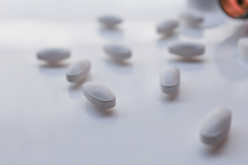 white pills on white blurred background having bottle, selective focus, blurred