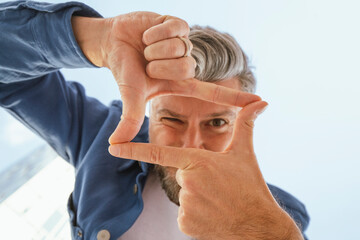 Man winking while looking through finger frame