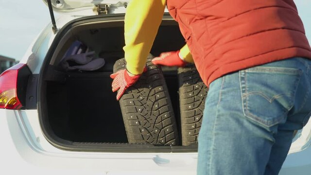 A man in warm clothes puts in a car trunk studded winter tires