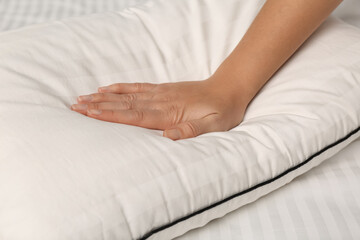 Woman touching soft pillow on bed, closeup
