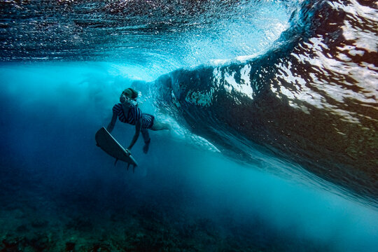 Woman with surfboard diving under waves