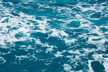 Water surface abstract background. White waves and foam on the blue sea water. Wake behind ship