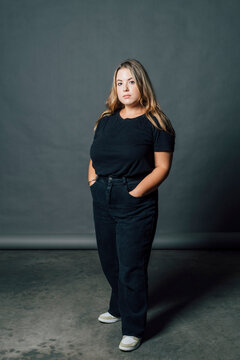 Plus size woman standing with hands in pockets by gray backdrop