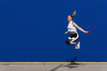 Female athlete jumping rope in front of blue wall