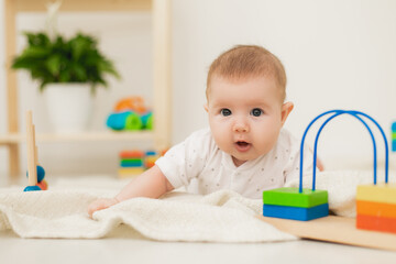 cute baby is lying on his stomach on a gray linen blanket and playing with colored educational toys. products for children. concept of a happy childhood and motherhood. child care. space for text