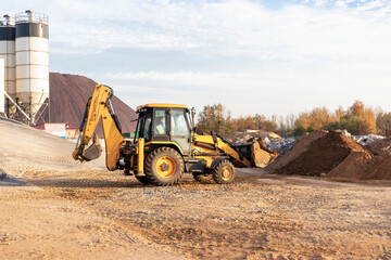 An excavator in the front bucket removes soil for backfill at the construction site. Construction equipment for earthworks.