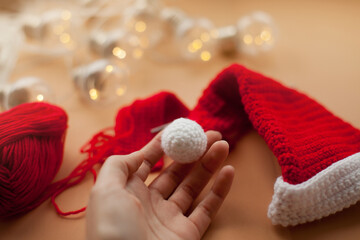 hand holding a crochet santa hat and christmas lights on beige background