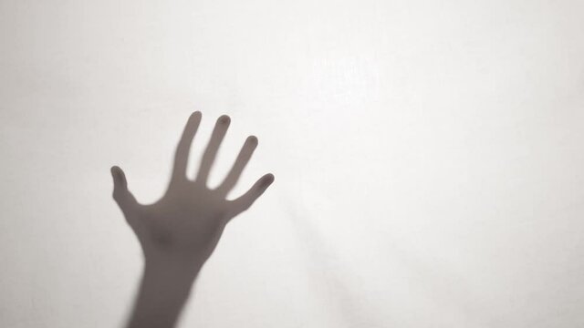 Ghostly hand shadow silhouette reaching out behind a white sheet. Halloween background
