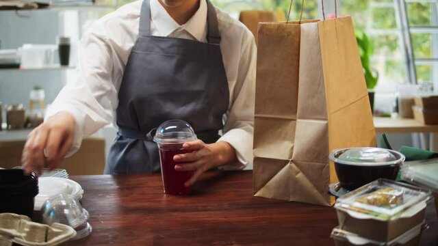 Food delivery service. Woman closing drink and taking paper bag with lunch boxes. Preparing take away meals. Healthy eating habits. Online contactless food shopping.