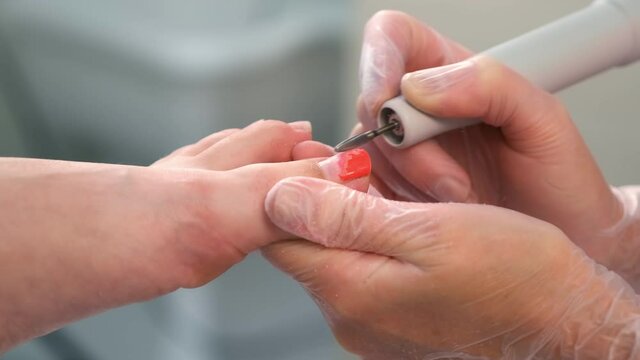 Pedicurist woman removes shellac polish from toes using manicure machine, closeup view. Pedicure Master is removing red gel polish from nails on toes using electric nail drill in cosmetology.
