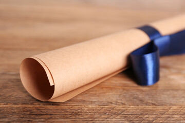 Rolled student's diploma with blue ribbon on wooden table, closeup