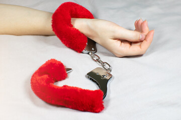 Woman wearing Red sexy fluffy handcuffs on her wrists in bed.