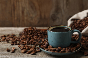 Cup of aromatic coffee and beans on wooden table. Space for text
