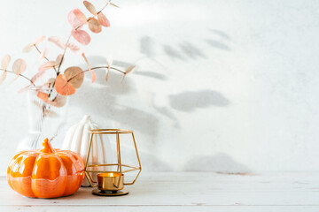 Details of Still life, pumpkins, candle, brunch with leaves on white table background, home decor in a cozy house. Autumn weekend concept. Fallen leaves and home decoration