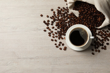 Cup of aromatic coffee and beans on light wooden table, flat lay. Space for text