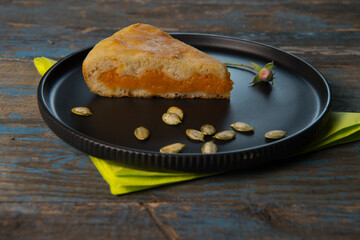 A piece of homemade pumpkin pie baked for the holiday on a black plate.