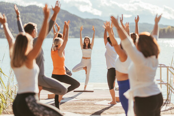 Female instructor teaching Vrikshasana to men and women during yoga class