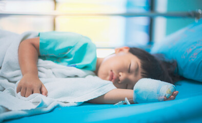 Obraz na płótnie Canvas Sick asian little child boys hand who have saline intravenous (iv) drip bandage is sleeping on bed in the hospital 