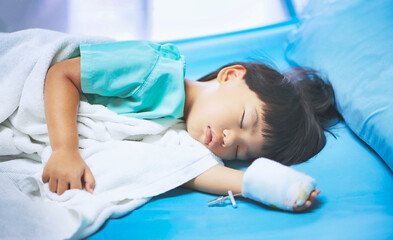 Obraz na płótnie Canvas Sick asian little child boys hand who have saline intravenous (iv) drip bandage is sleeping on bed in the hospital 