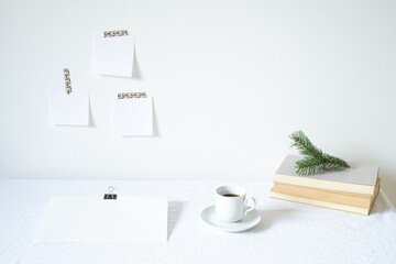 Christmas or New Year breakfast scene. Notepad mockup of good intentions. Blank note paper hanging on the wall.Books, coffee cup, empty paper sheet on the desk.Working space, home office concept