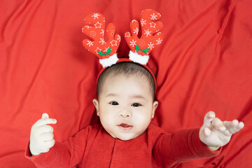New year and Christmas concept.Headshot of 5 months old cute newborn baby boy wearing christmas antlers of a deer on a red blanket.Looking at camera. Holiday season.