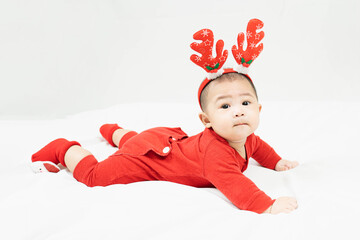 New year and Christmas concept with 5 months old cute newborn baby boy wearing christmas antlers of a deer,red clothes lying on the bedsheet at home.Looking at camera. Holiday season.