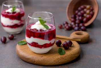 Eton Mess. Layered dessert with whipped cream and red berries served in two glasses, decorated with mint leaves. Dark background, selective focus. 
