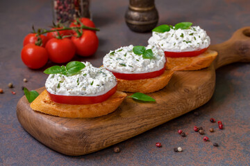 Fototapeta na wymiar Fresh Tomato Bruschetta topped with Herbed Ricotta and basil leaves served on wooden board. Dark background, selective focus. 