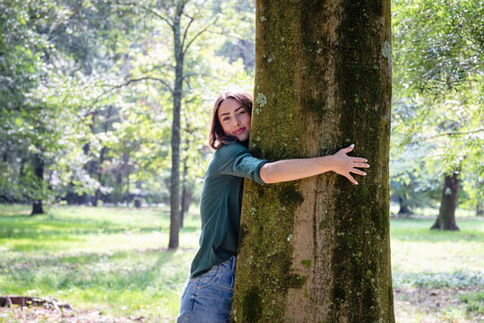 Beautiful young woman hugging tree in park