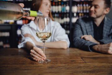 Closeup waiter pours white wine into glass. Fun couple man and woman laughing in restaurant on first date