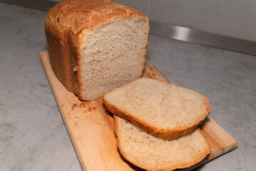 Loaf of fresh bread and two pieces of bread with bread crumbs on wooden board
