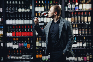 Portrait sommelier man with glass of red wine on background of showcase of alcohol store