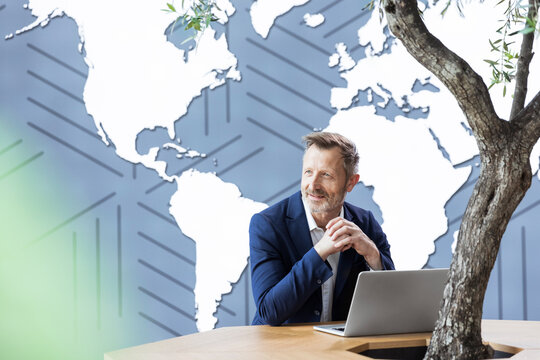 Smiling businessman with hands clasped sitting at desk in office