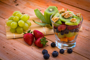 Fresh seasonal fruit salad in a glass on wooden rustic table. Healthy nutrition with papaya, kiwi, banana, strawberry, blueberry, walnuts and white grape