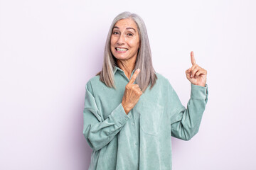middle age gray hair woman smiling happily and pointing to side and upwards with both hands showing...