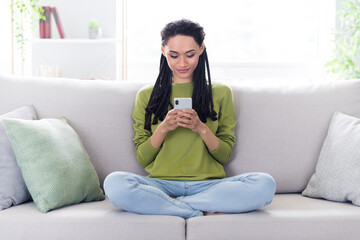 Obraz premium Full body photo of calm peaceful afro american woman sit sofa look hold phone indoors inside house home