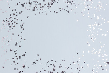 Border frame made of silver colored stars confetti on a blue pastel background.