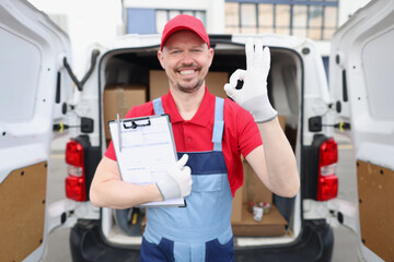 Smiling man courier showing ok gesture on background of truck with cardboard boxes