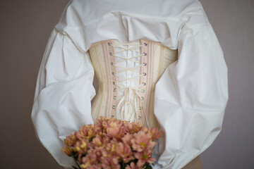 a girl in a white shirt and beige corset holds flowers in her hands