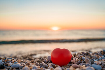 Beautiful pebbles and a red heart on a quiet calm beach at sunset. The concept of serenity and relaxation. Summer vacation at the sea
