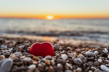 Beautiful pebbles and a red heart on a quiet calm beach at sunset. The concept of serenity and relaxation. Summer vacation at the sea
