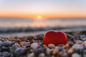 Beautiful pebbles and a red heart on a quiet calm beach at sunset. The concept of serenity and relaxation. Summer vacation at the sea
