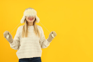 Attractive girl in fur cap and sweater on yellow background