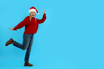 Fototapeta na wymiar Attractive woman in sweater and Santa hat on blue background