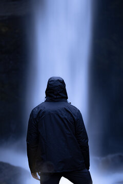 Unrecognizable man standing near rapid waterfall flowing through rocky cliff