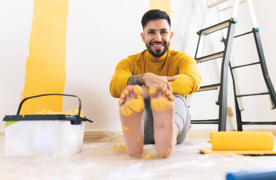 Happy handsome man with yellow paint on foot sitting at home