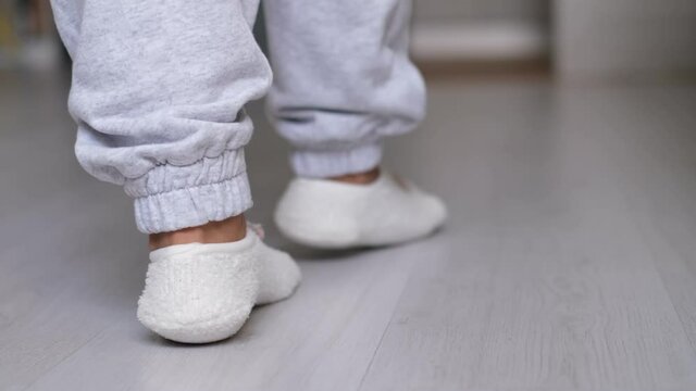 Legs of a woman in socks walking on the wooden floor of her house with a sofa in the background. feet wearing white socks on gray wooden floor