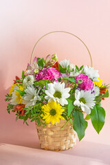 A basket with a bouquet of flowers. Roses and chrysanthemums in a basket on a pink background. A...
